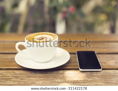 Cup of cappuccino and cell phone on a wooden table