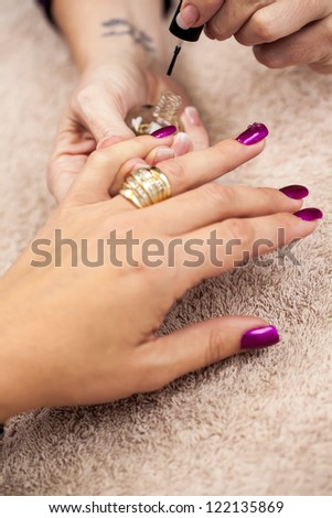 The beautician busy with the final touches of the manicure, putting on the cutex.