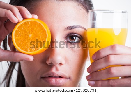 A young woman with orange skin in her left and orange juice in her right hand.