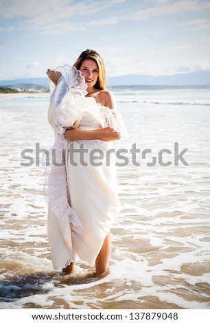 beautiful young caucasian woman playing in the sea wearing an ivory evening gown