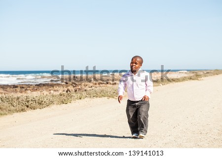 dwarfish african man walking down the dirt road along the rocky coast