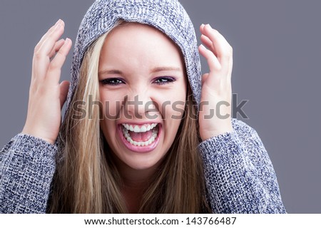 a pretty caucasian girl with blond hair wearing a hooded jersey raising her hands to her head and yelling in a sense of humor