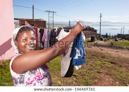 image of an african woman hanging her clean laundry in the sunny outdoors with a proud smirk on her face