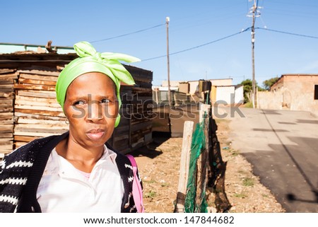 an image of an african woman standing by the fence wearing a lime green bandanna pulling her face in a pout