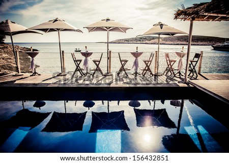 image of small tables under umbrellas on the deck looking out on the sea canals with a bright swimming pool in front of them