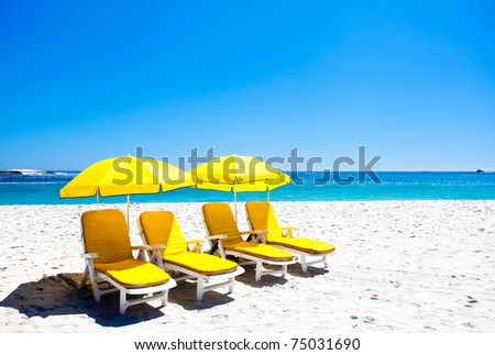 Four yellow beach chairs under two umbrellas on the beach.