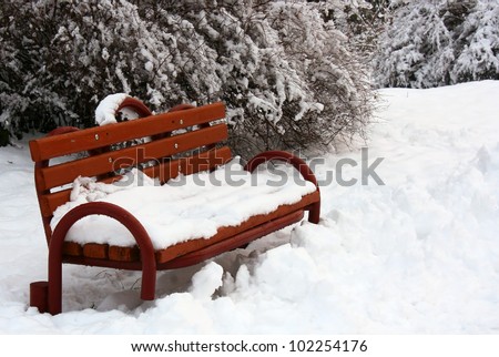 Snow-covered bench in winter park