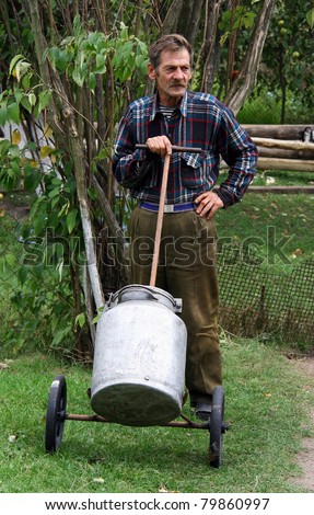 Man in checkered shirt standing and holding a cart with containers for water