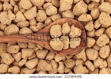 Soy protein chunks in an olive wood spoon and forming a background.