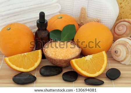 Orange fruit with spa accessories of white towels, stones, sea salt, aromatherapy essential oil bottle, sponge and sea shells over bamboo background.