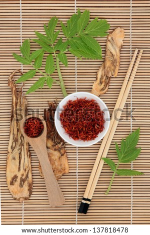 Chinese herbal medicine of saffron spice and angelica herb root with leaf sprigs over bamboo background.