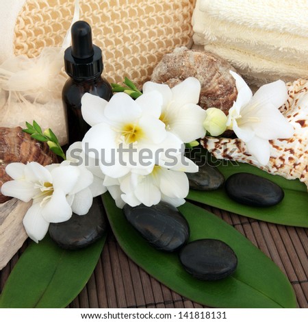 Spa and aromatherapy accessories with freesia flower arrangement, leaf sprigs and shells over bamboo background.