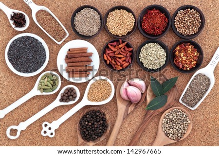 Spice and herb selection spoons, bowls and measuring scoops over cork background.