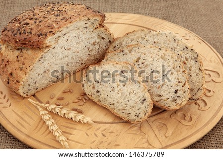 Seeded brown bread loaf on beech wood board with wheat over hessian background.