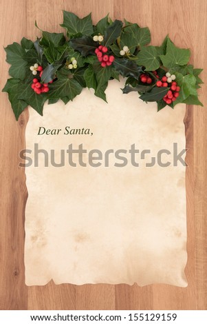 Letter to santa claus on old parchment paper with border of holly, ivy and mistletoe over oak background.