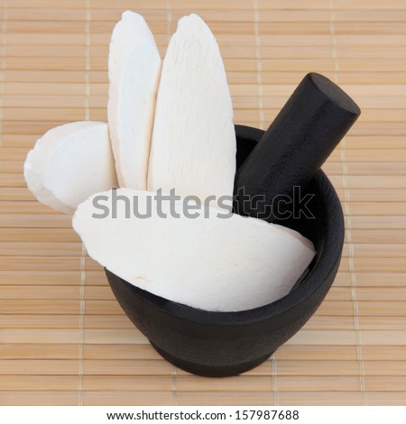 Discoria used in chinese herbal medicine in a black stone mortar with pestle over bamboo. Shan yao. Discorea opposita.