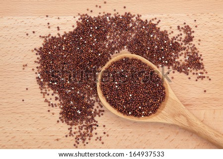 Organic quinoa grain in a wooden spoon over beech wood board.