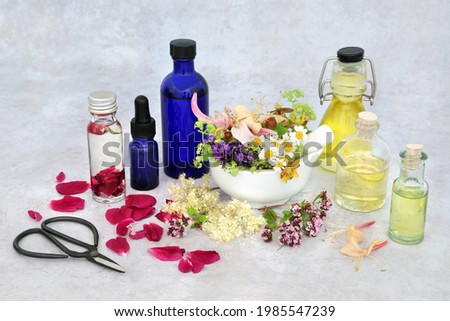 Summer herb and flower selection for preparing aromatherapy essential oils with oil bottles and flowers in a mortar with pestle and loose. Herbal plant medicine health care concept.