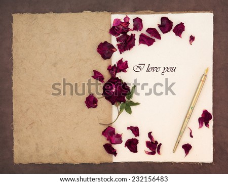 Old fashioned vintage notebook,with I love you phrase, ink pen and red rose with petals over lokta paper background.