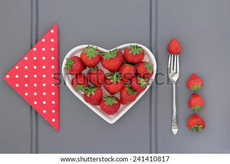 Strawberry fruit in a heart shaped dish with polka dot napkin and old silver fork.