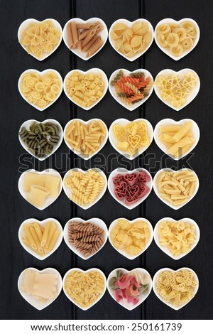 Large pasta food selection in heart shaped porcelain dishes over dark wood background.