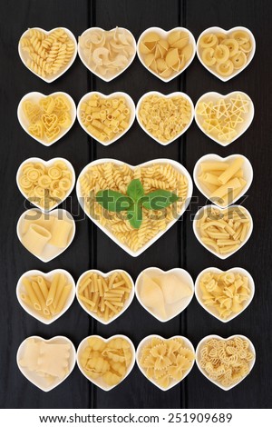 Large pasta food selection in heart shaped porcelain dishes with basil herb over dark wood background.