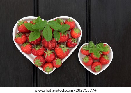Strawberry fruit in heart shaped porcelain dishes over dark wood background,.