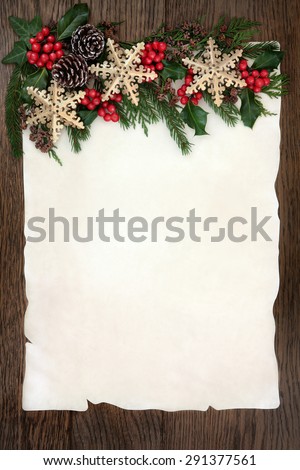 Christmas background border with gold snowflake bauble decorations, holly, ivy, cedar cypress and fir on parchment paper over old oak wood.