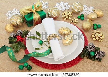 Christmas dinner still life with place setting, plates, napkin, baubles, ribbons and gift box with winter flora over oak background.