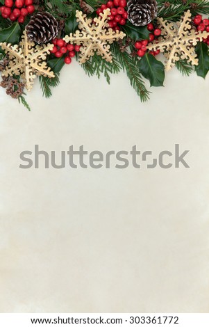 Christmas abstract background border with gold snowflake decorations, holly, fir and cedar cypress greenery over parchment paper.