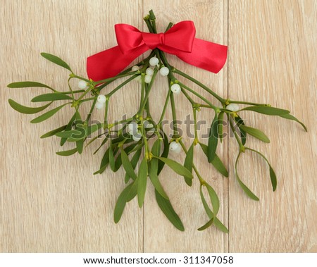 Mistletoe with red ribbon bow over light oak wood background.