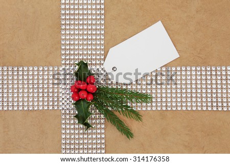 Christmas gift wrapping with diamond bling ribbon, tag and holly over hemp paper background.
