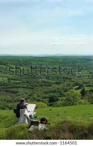 Artist sitting in a chair, next to his artists equipment, starting to draw the  landscape of fields and trees. Set in the Cambrian mountains, Wales, United Kingdom.