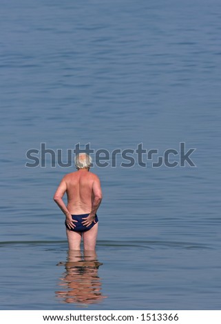 Elderly man in blue swimming trunks standing in the sea about to swim.