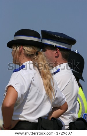 British police in uniform, with a blonde female policewoman to the foreground. Set against a blue sky.