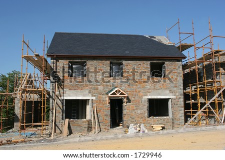 New house with a sandstone facade, under building construction with scaffolding erected to the side, set against a blue sky.