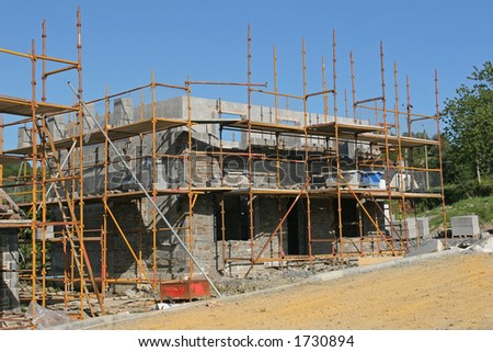 New house under building construction with scaffolding erected in the front and to the side, set against a blue sky.