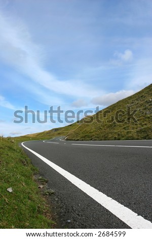Uphill road in deserted countryside with grass verges either side with a blue sky with clouds. Set in the Brecon Beacons, National Park, Wales, United Kingdom.
