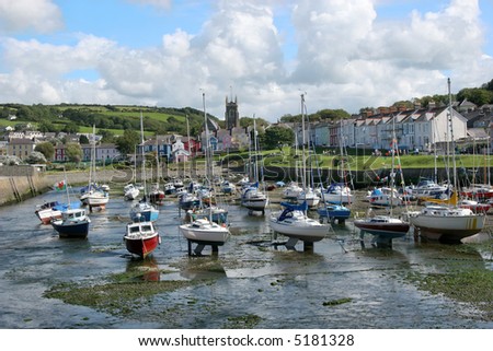 Sailing boats at anchor in a small harbor with the tide out and colorful houses to the rear. Location Aberaeron, Wales, United Kingdom.