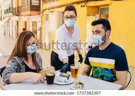 Clients with masks on the terrace of a bar in Spain attended by a waiter with gloves and masks. Social distancing
