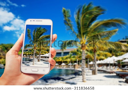 Nice view of the sea with palm trees on the screen. Phone in the hand.