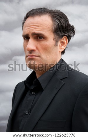 portrait of young man with black curly hair,in elegant suit,gray clouds background