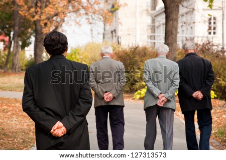 age difference, young man in the suit walking behind seniors,with both hands on his back,thinking about ,passing of life