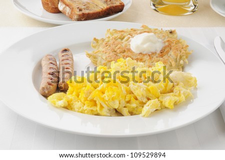 Breakfast of link sausage, scrambled eggs and potato pancakes topped with sour cream