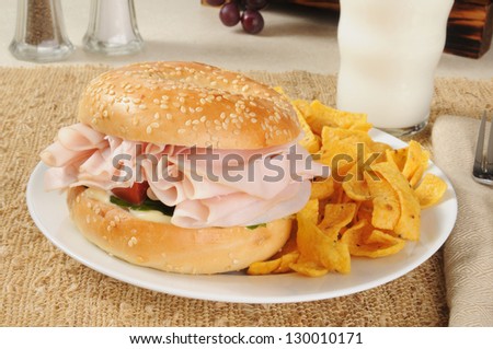 A ham sandwich on a bagel with corn chips