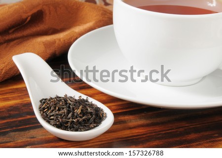 A cup of black tea with whole leaf tea in a spoon