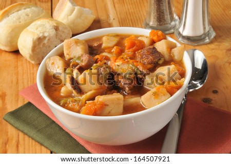 A bowl of vegetable beef soup with a dinner roll