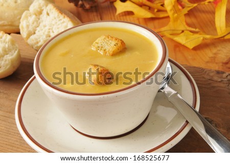 A cup of butternut squash soup with rolls