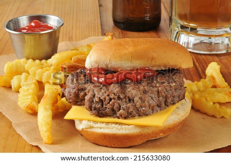 A thick hamburger with cheese, french fries and a mug of beer on a rustic wooden bar counter