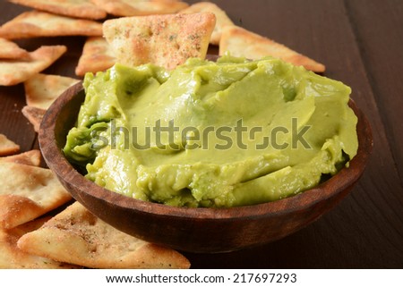 A wooden bowl of guacamole with toasted, seasoned pita chips